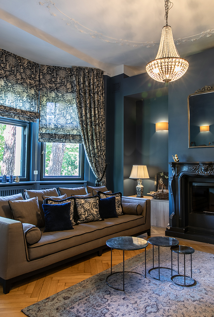 Eleganter Wohnraum mit Raffrollos, Vorhängen und Kissen im klassischen Muster, kombiniert mit dunklen Wänden und luxuriösen Details.